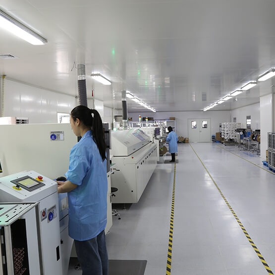 SMT (Surface Mount Technology) production line with technician in blue uniform operating equipment in clean room facility.